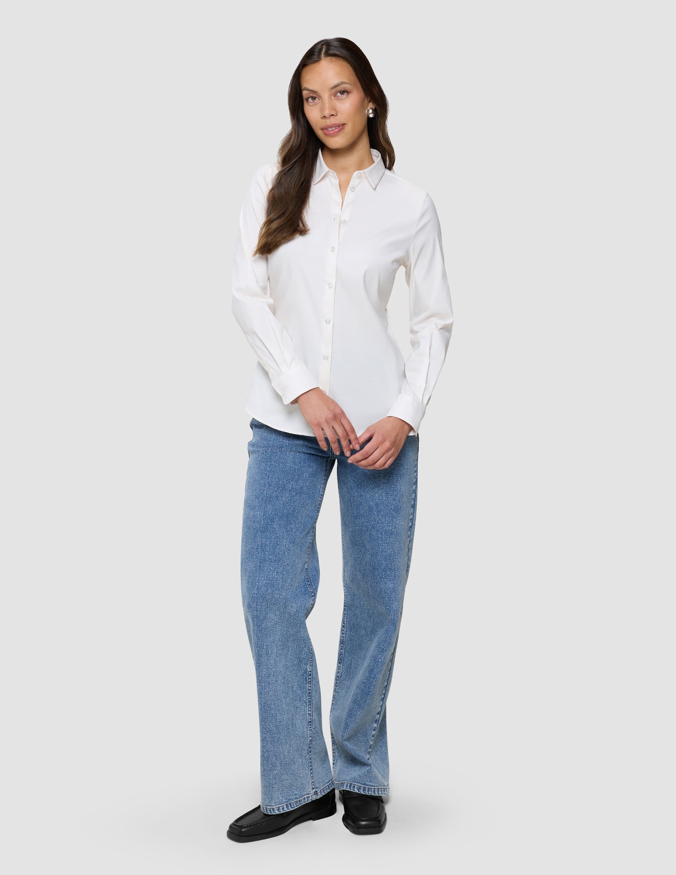 En kvinde iført en »Women’s Oxford Shirt White Orchid Slim«, blå jeans og sorte loafers.